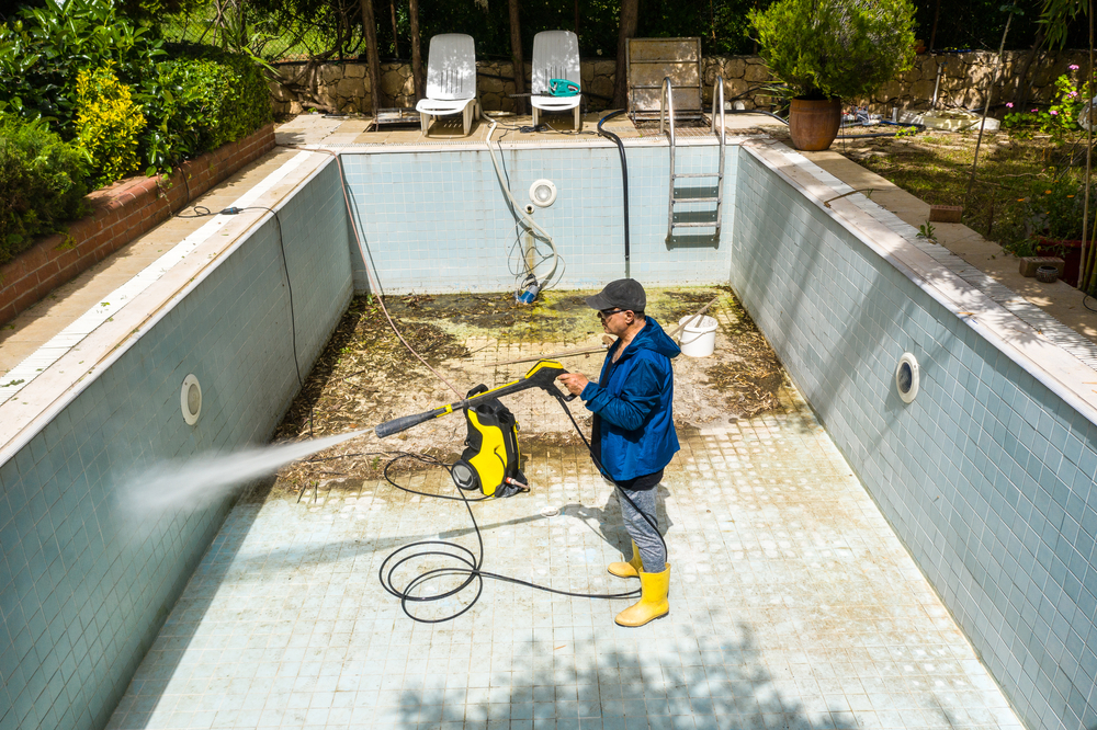 A service man is cleaning the pool ground with a pressure pump