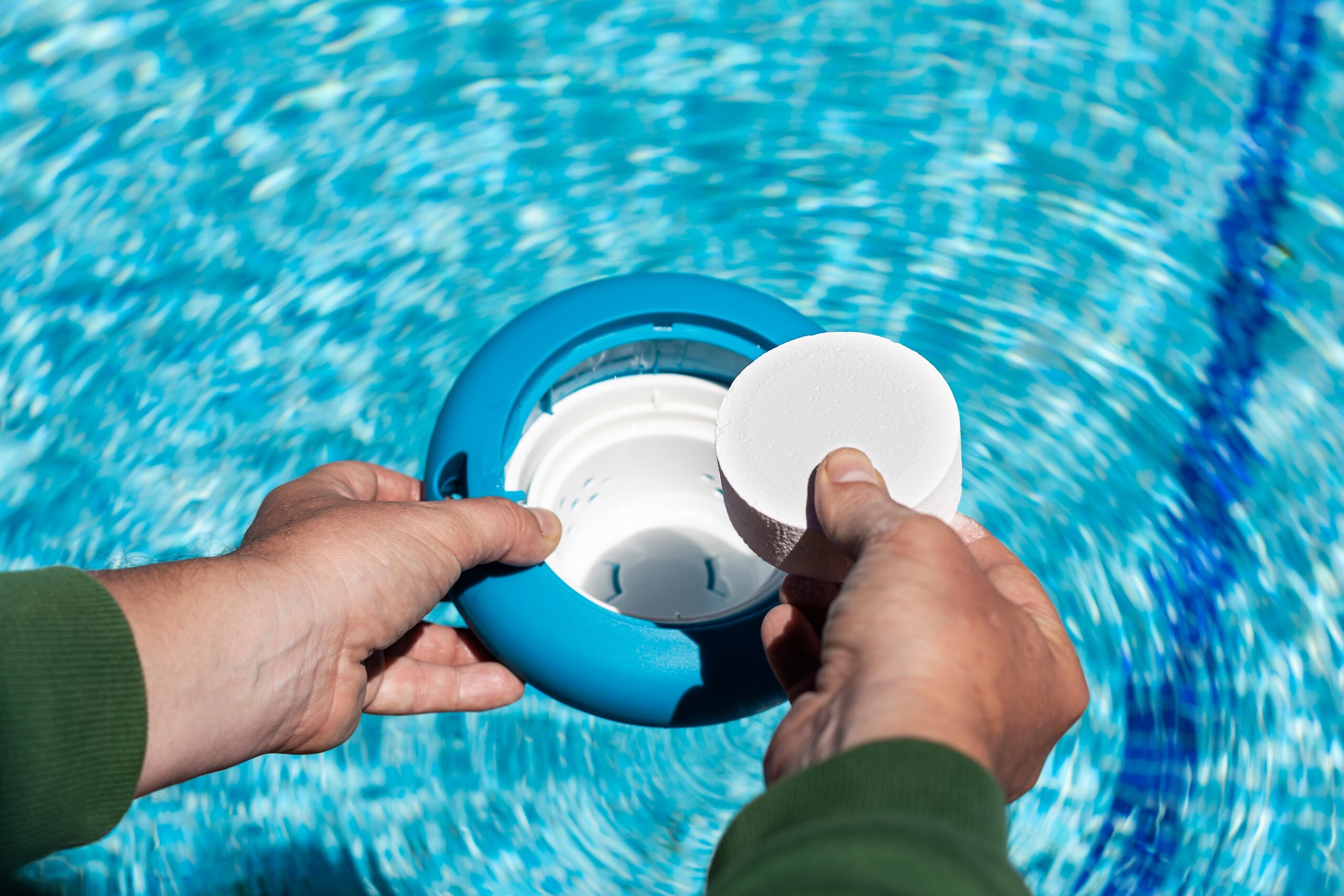 Operator's hand introducing white chlorine tablets on the pool skimmer. Chlorine tablets for pool water. disinfection and prevention against the development of microbes. Floating dispenser for ch